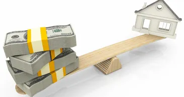 Stack of money and a toy house on a see-saw